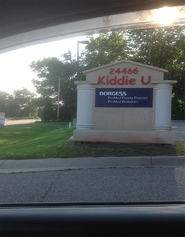 A blue sign on a concrete sign display situated in grass. Above the sign, in red lettering, it says: “24466 Kiddie U.” Blue sign with white text: 1st line, BORGESS (large text); 2nd line,  ProMed Family Practice (smaller text; and 3rd line, ProMed Pediatrics (smaller text).