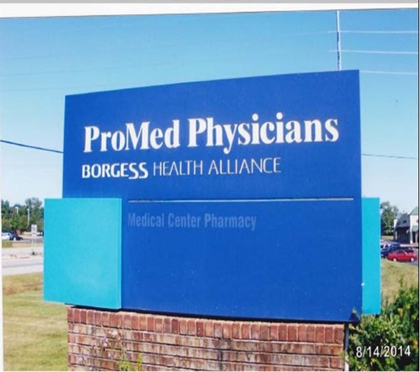 A blue sign on a brick with white text: 1st line, ProMed Physicians (large text); 2nd line, BORGESS HEALTH ALLIANCE (smaller text); and 3rd line, and in light blue: Medical Center Pharmacy (in light blue, even smaller text).