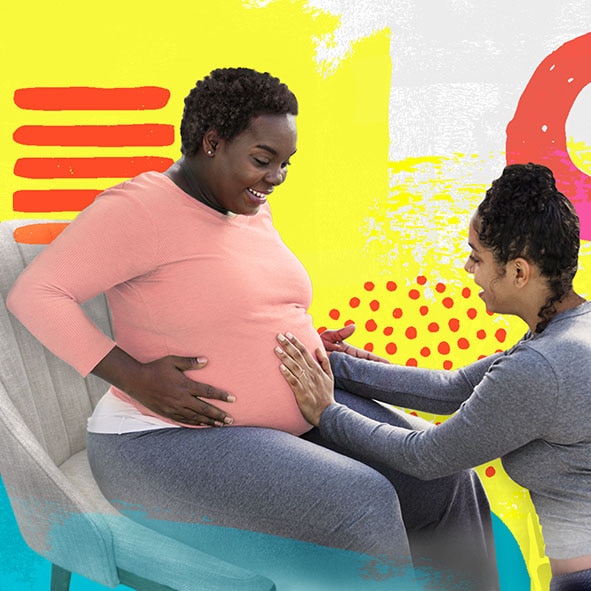 a female doula crouches down to feel a sitting pregnant woman's belly